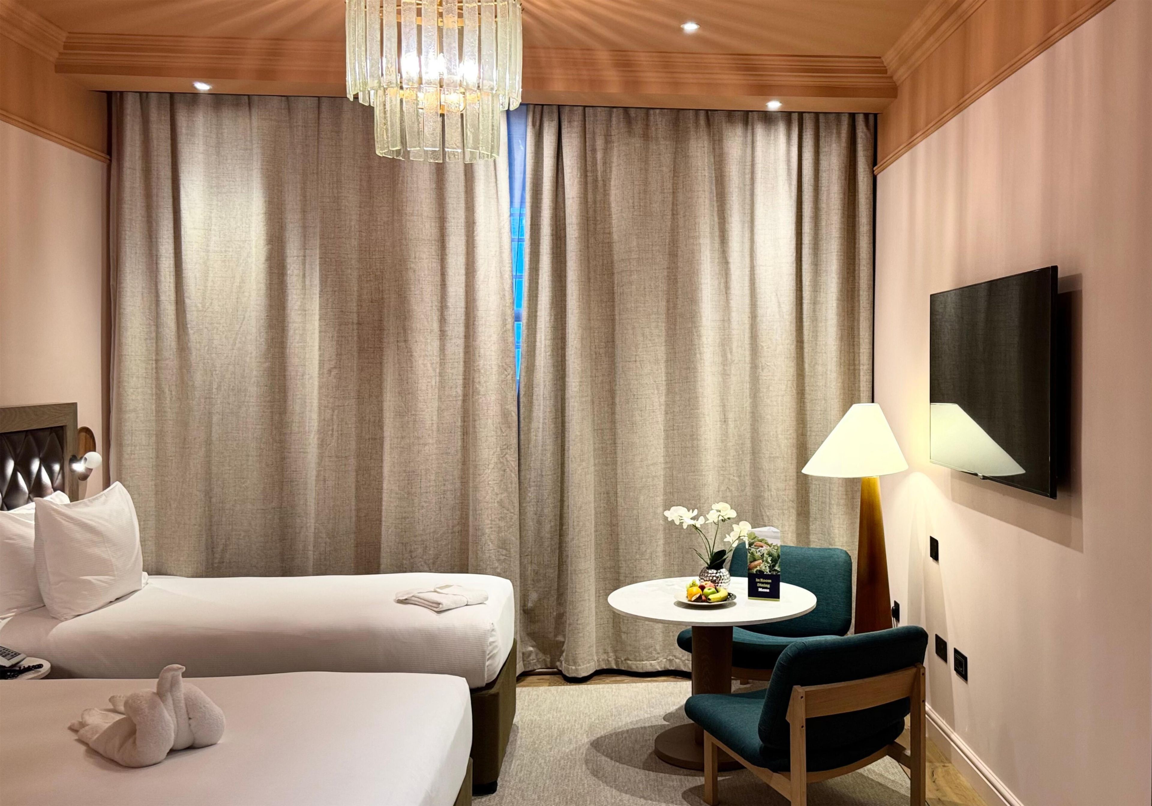 A hotel room with a bed, a chair, a table with a vase of flowers, and a television mounted on the wall.
