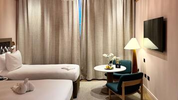 A hotel room with a bed, a chair, a table with a vase of flowers, and a television mounted on the wall.