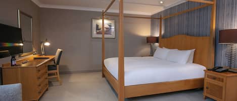 A four-poster bed with a wooden frame, a desk with a chair, a nightstand, and a television on the left side.