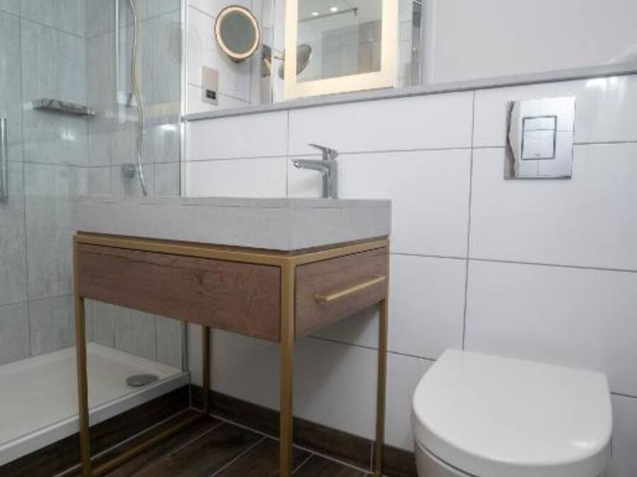 Un baño moderno con cabina de ducha de vidrio, tocador de madera con espejo y un inodoro blanco.