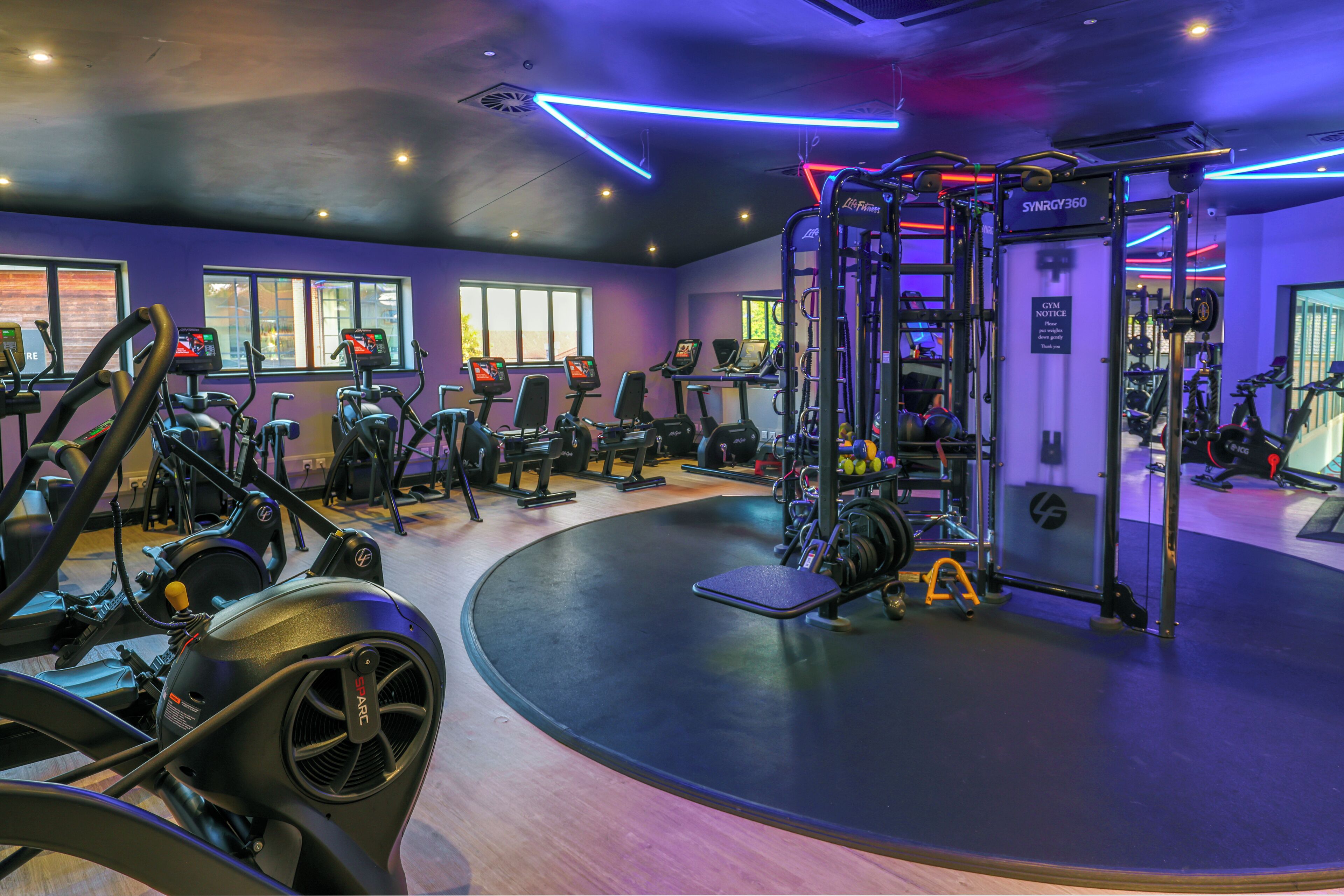 A gym with various exercise equipment, including treadmills and weight machines, and a wall-mounted squat rack.