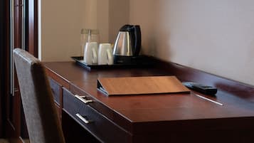 A hotel room desk with a coffee maker, mugs, and a remote control.