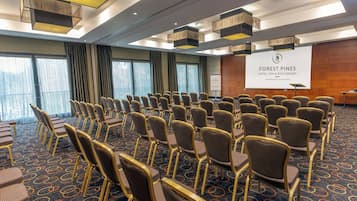 A conference room with rows of chairs, a projector screen, and a banner for Forest Pines Hotel & Spa Golf Resort.