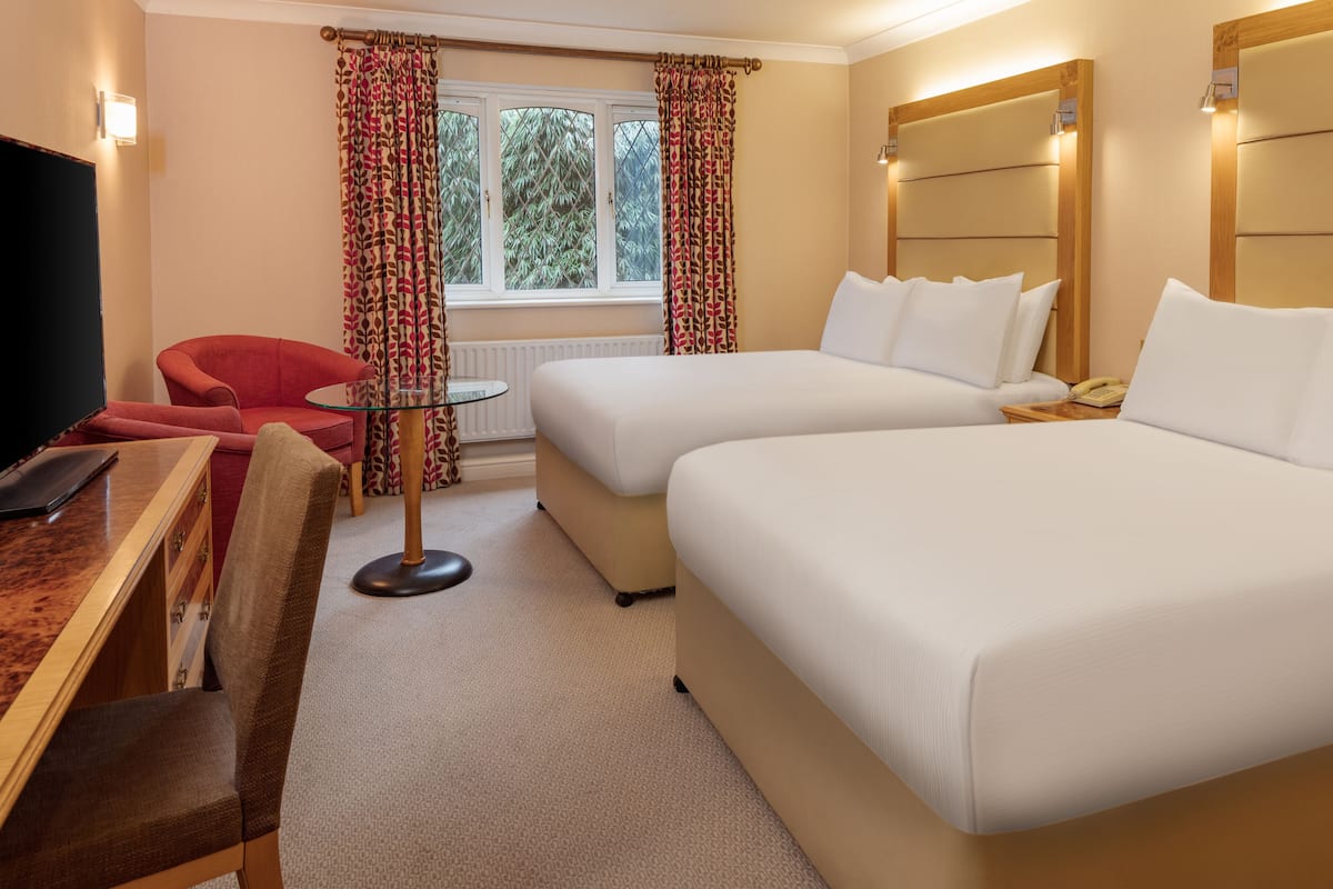 A hotel room with two beds, a desk with a chair, a TV, and a window with curtains.