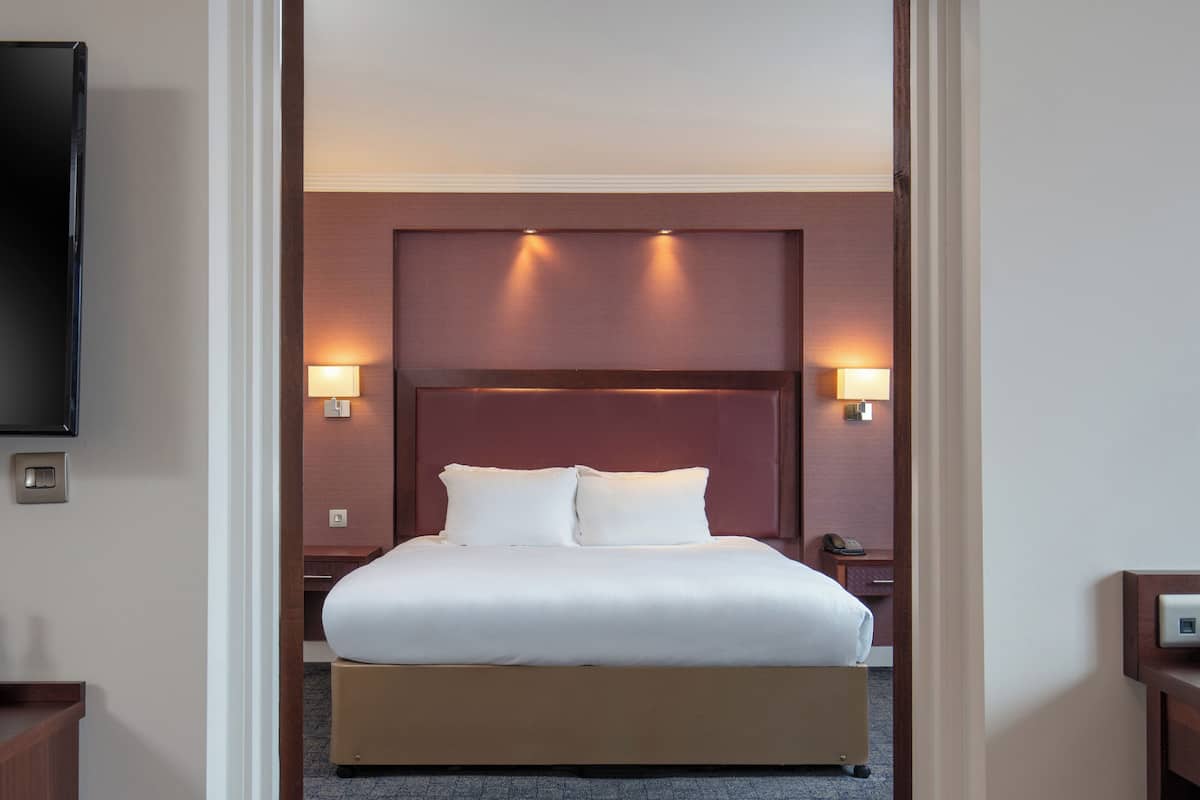 A hotel room with a large bed, two bedside lamps, a flat-screen TV, and a wall-mounted thermostat.