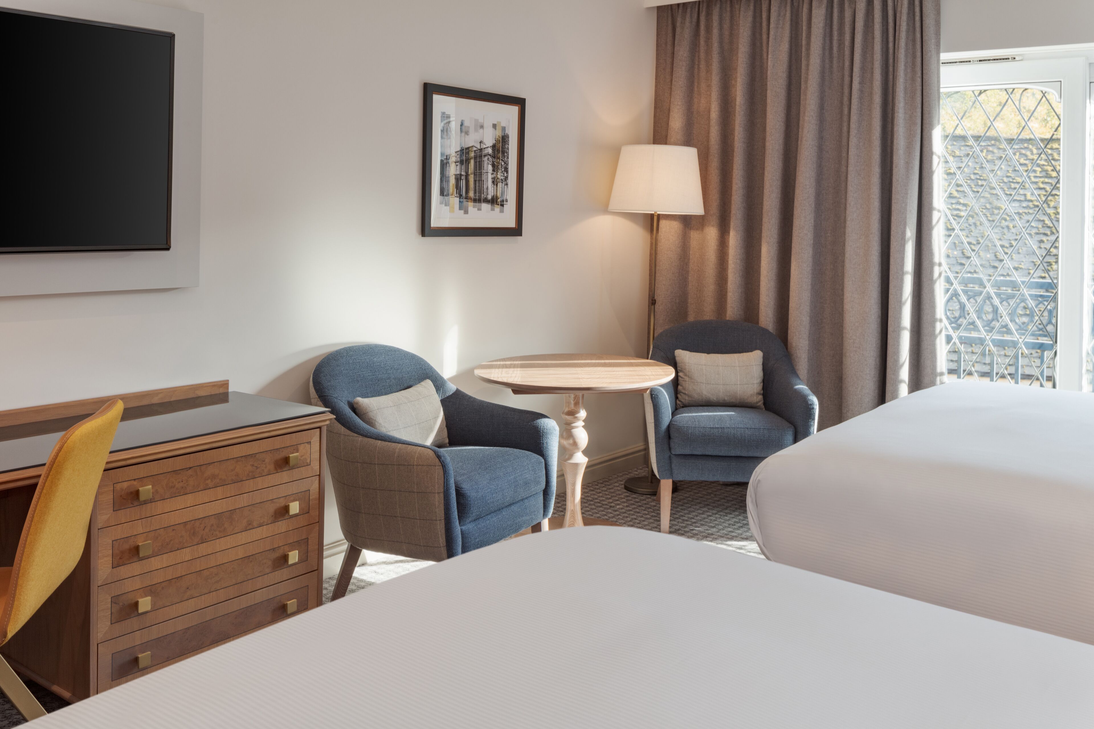 A hotel room with a bed, two armchairs, a desk, and a small table.