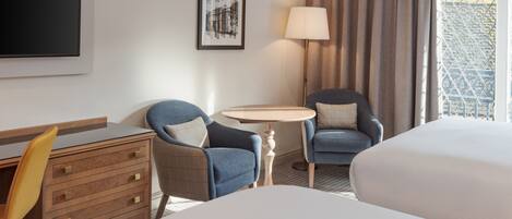 Ein Hotelzimmer mit einem Bett, zwei Sesseln, einem Schreibtisch und einem kleinen Tisch.