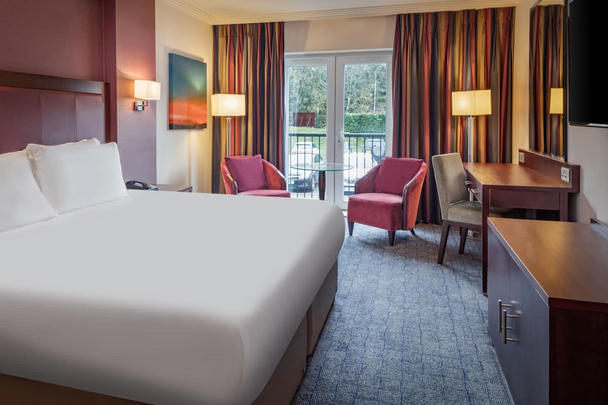 A hotel room with a large bed, two armchairs, a desk, and a TV.