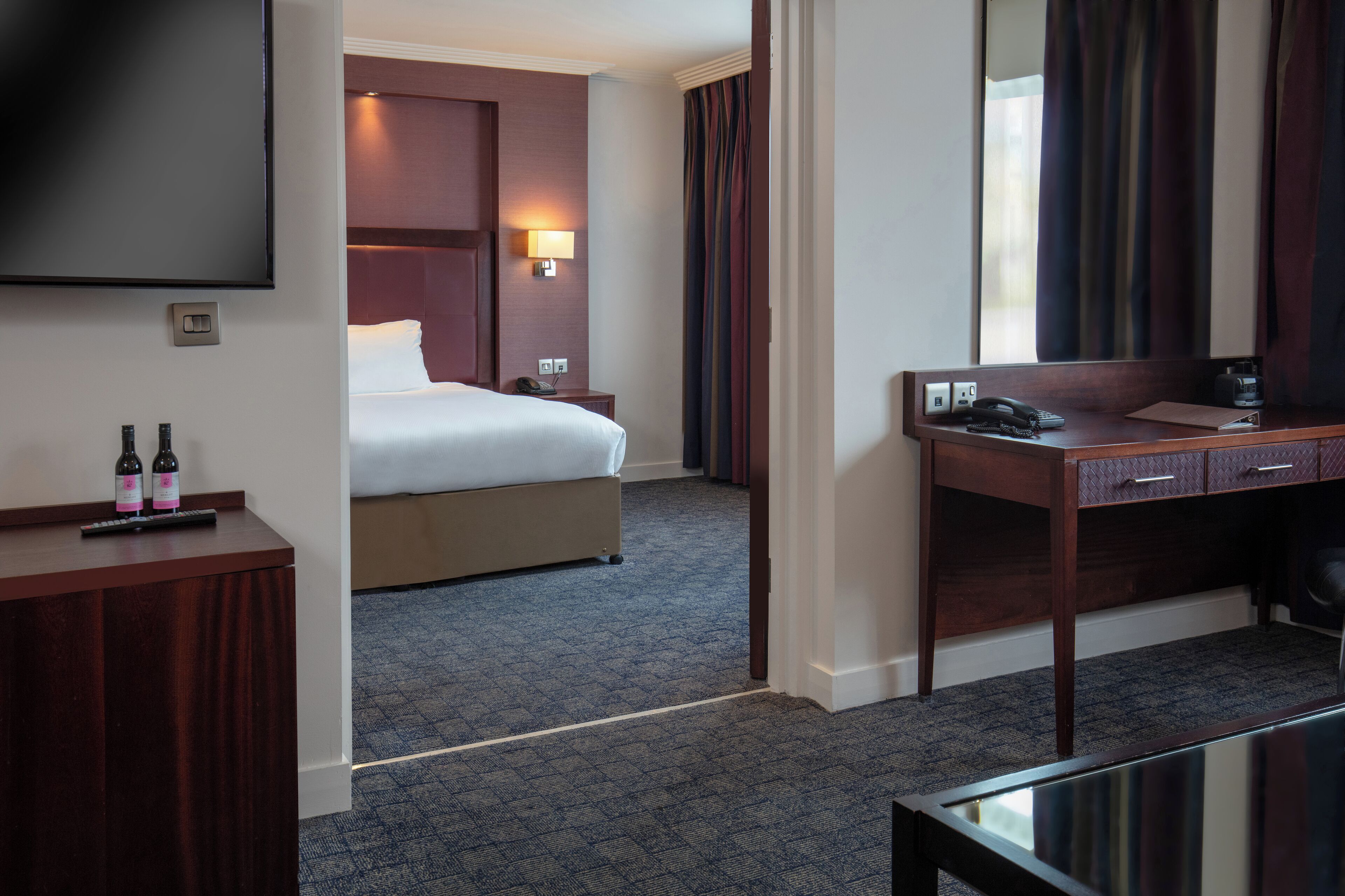 Quarto de hotel com cama, escrivaninha, televisão e minibar.