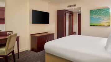 A hotel room with a bed, a desk with a chair, a television, a wardrobe, and a painting on the wall.
