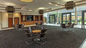 A spacious lobby with a reception desk, seating area, and large windows offering a view of the outdoors.