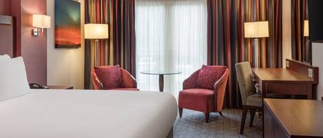 A hotel room with a large bed, two armchairs, a desk, and a television.