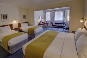 A hotel room with three beds, a desk, a chair, and a sofa.