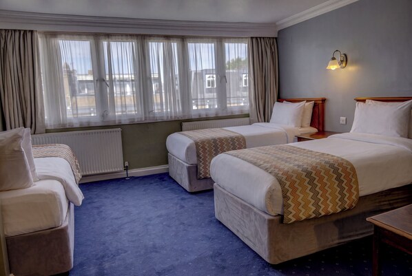 Habitación de hotel con dos camas, un escritorio, una silla, un radiador y una ventana con cortinas.