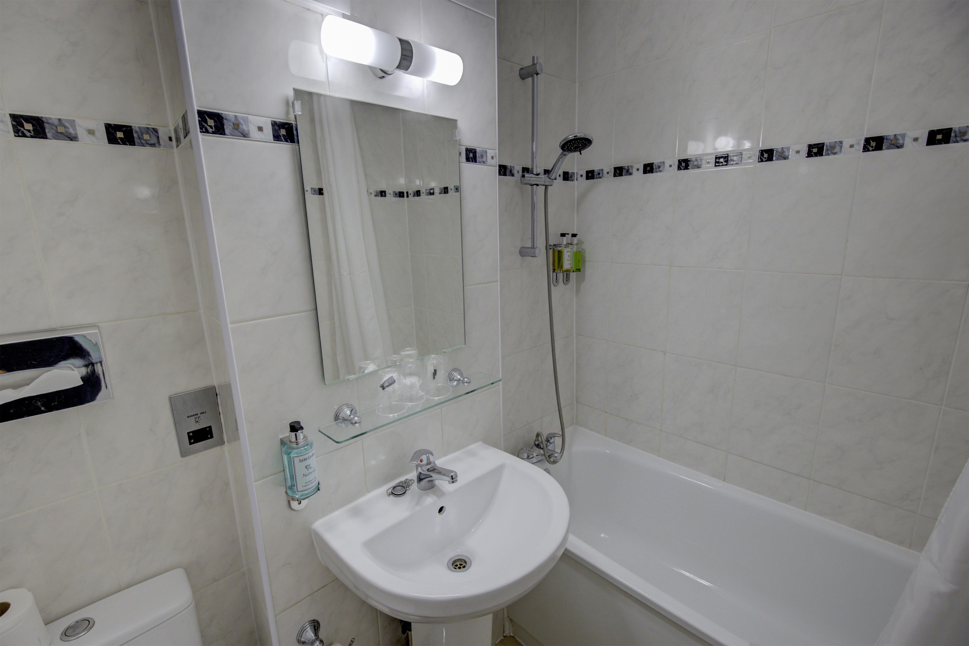 Un baño con lavabo blanco, espejo, ducha e inodoro.