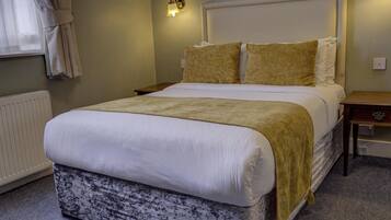 A neatly made bed with a white duvet and a beige throw blanket, a bedside table with a lamp, and a wall-mounted light fixture.