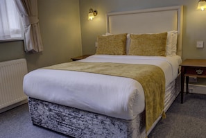 A neatly made bed with a white duvet and a beige throw blanket, a bedside table with a lamp, and a wall-mounted light fixture. - Best Western Swiss Cottage Hotel (London)