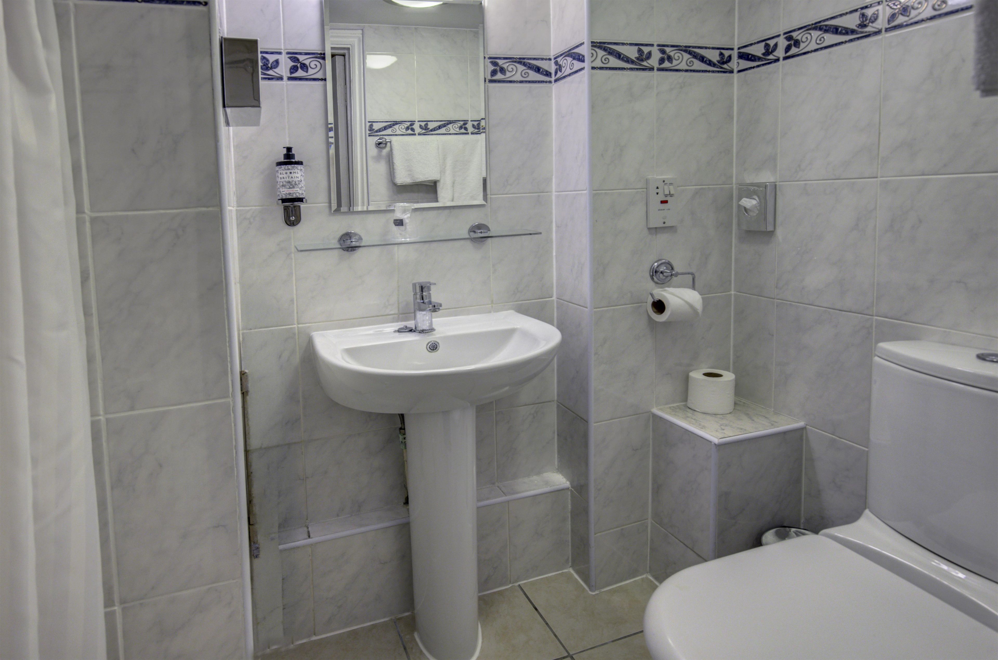 Een badkamer met een witte wastafel, een spiegel, een toilet en een rol toiletpapier op een klein plankje.