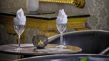 A dining table with two crystal glasses and a decorative bowl, set against a backdrop of a mirror and ornate wall decorations.