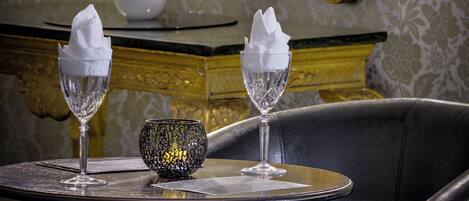 Una mesa de comedor con dos copas de cristal y un cuenco decorativo, frente a un espejo y ornamentos en la pared.