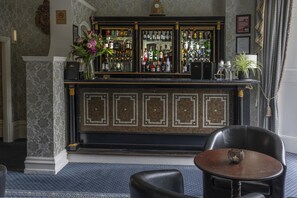 A bar area with a tiled backsplash, a variety of liquor bottles, and a black leather chair with a decorative bowl on the table. - Best Western Swiss Cottage Hotel (London)