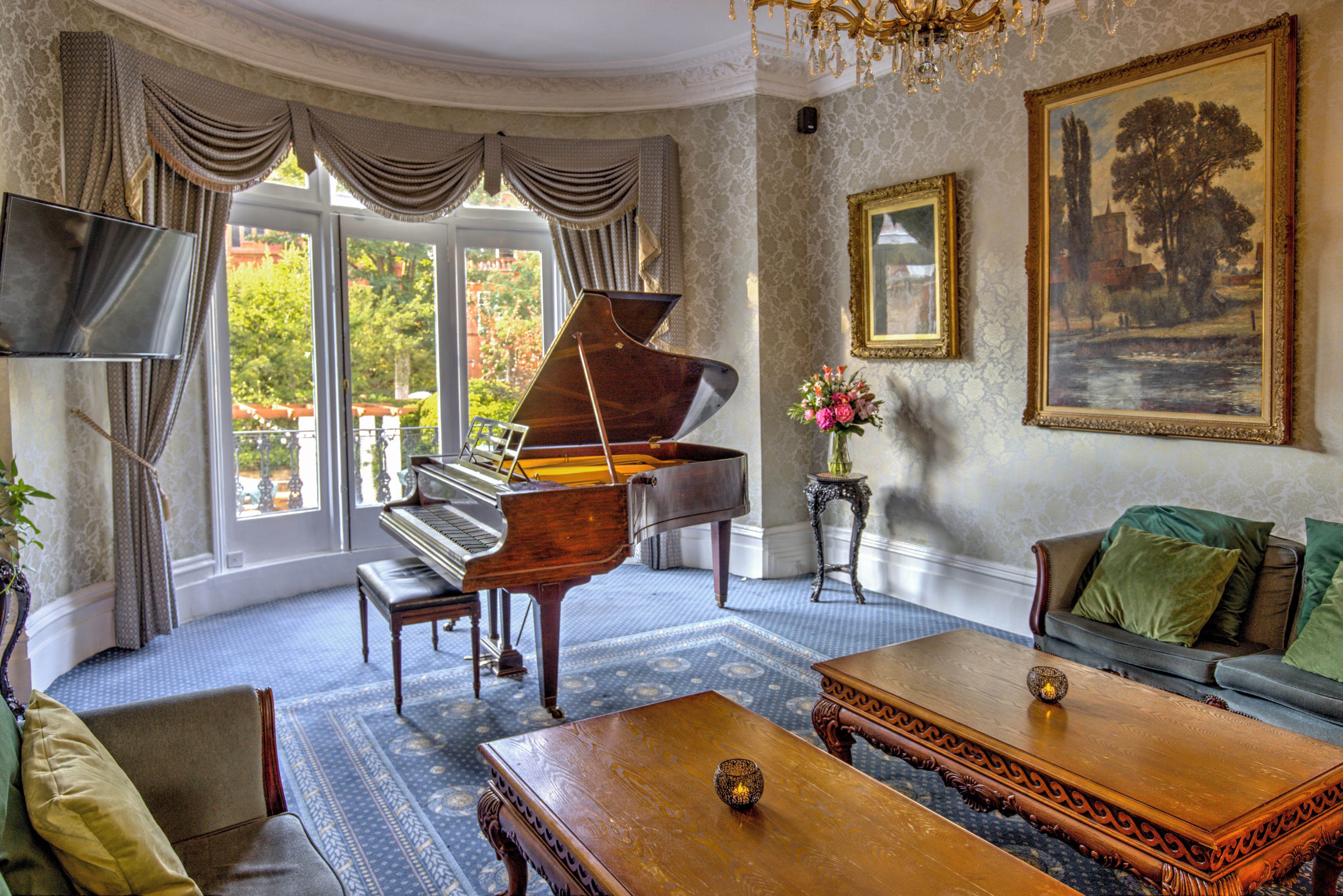 Un piano de cola en una habitación amplia con un gran ventanal, un sofá, una mesa de centro y un cuadro en la pared.