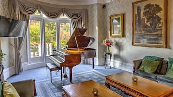 Un piano de cola en una habitación amplia con un gran ventanal, un sofá, una mesa de centro y un cuadro en la pared.
