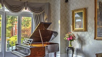A grand piano in a room with a chandelier, a painting, and a view through a window.
