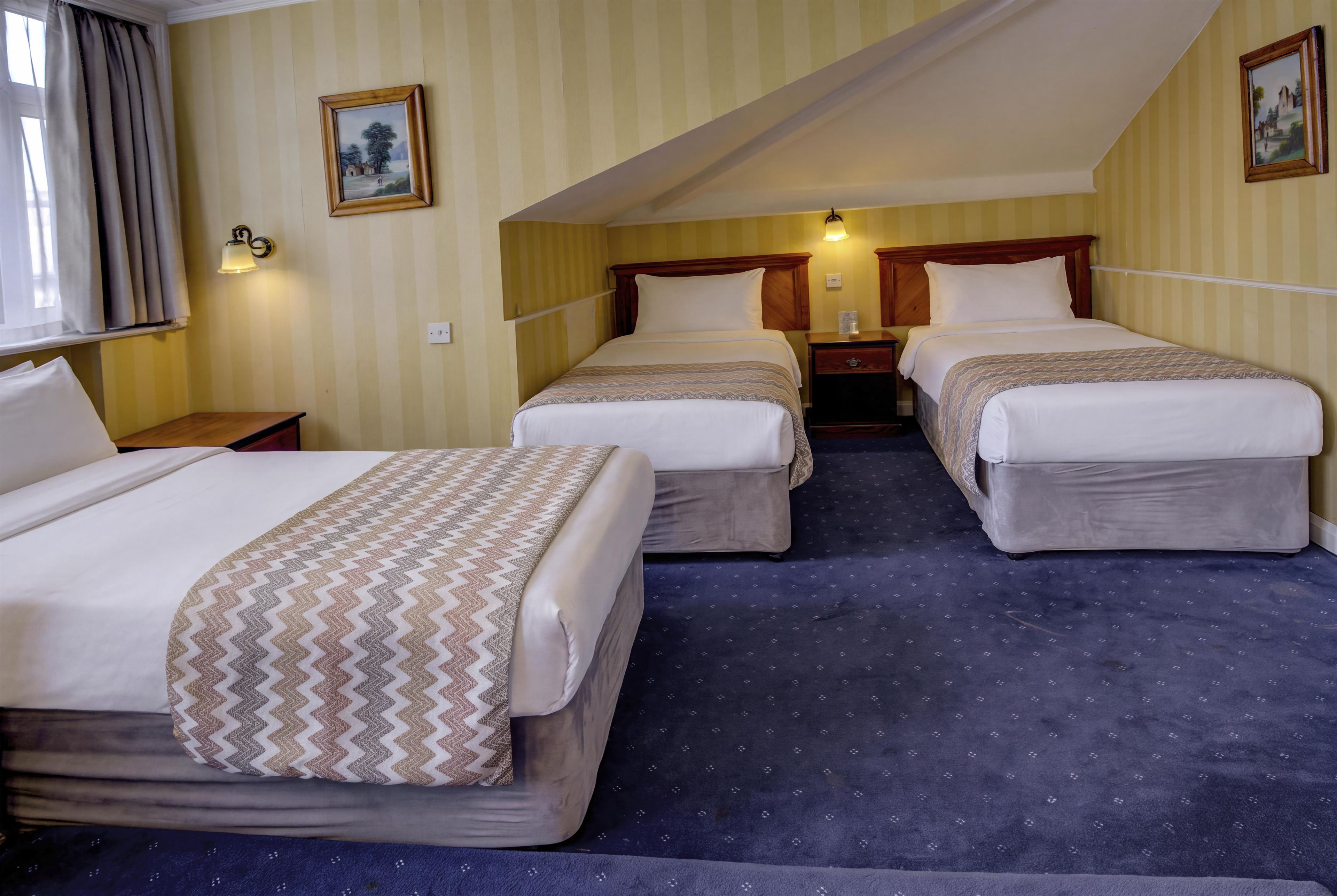 A hotel room with two beds, a nightstand, a lamp, and a window with curtains.