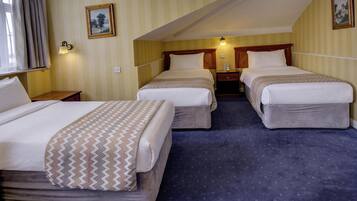 A hotel room with two beds, a nightstand, a lamp, and a window with curtains.