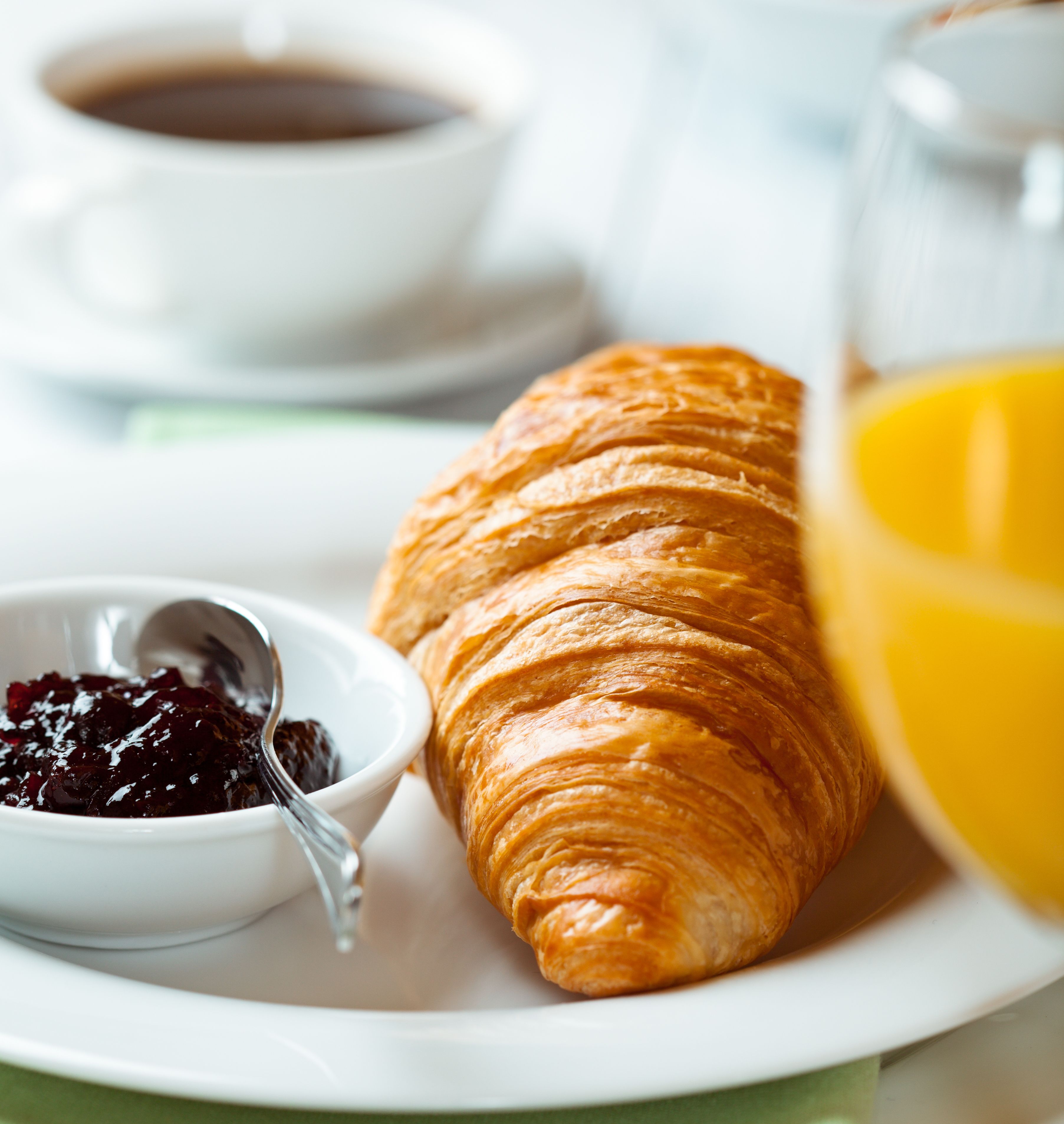 A croissant, a bowl of jam, a cup of coffee, and a glass of orange juice on a plate.