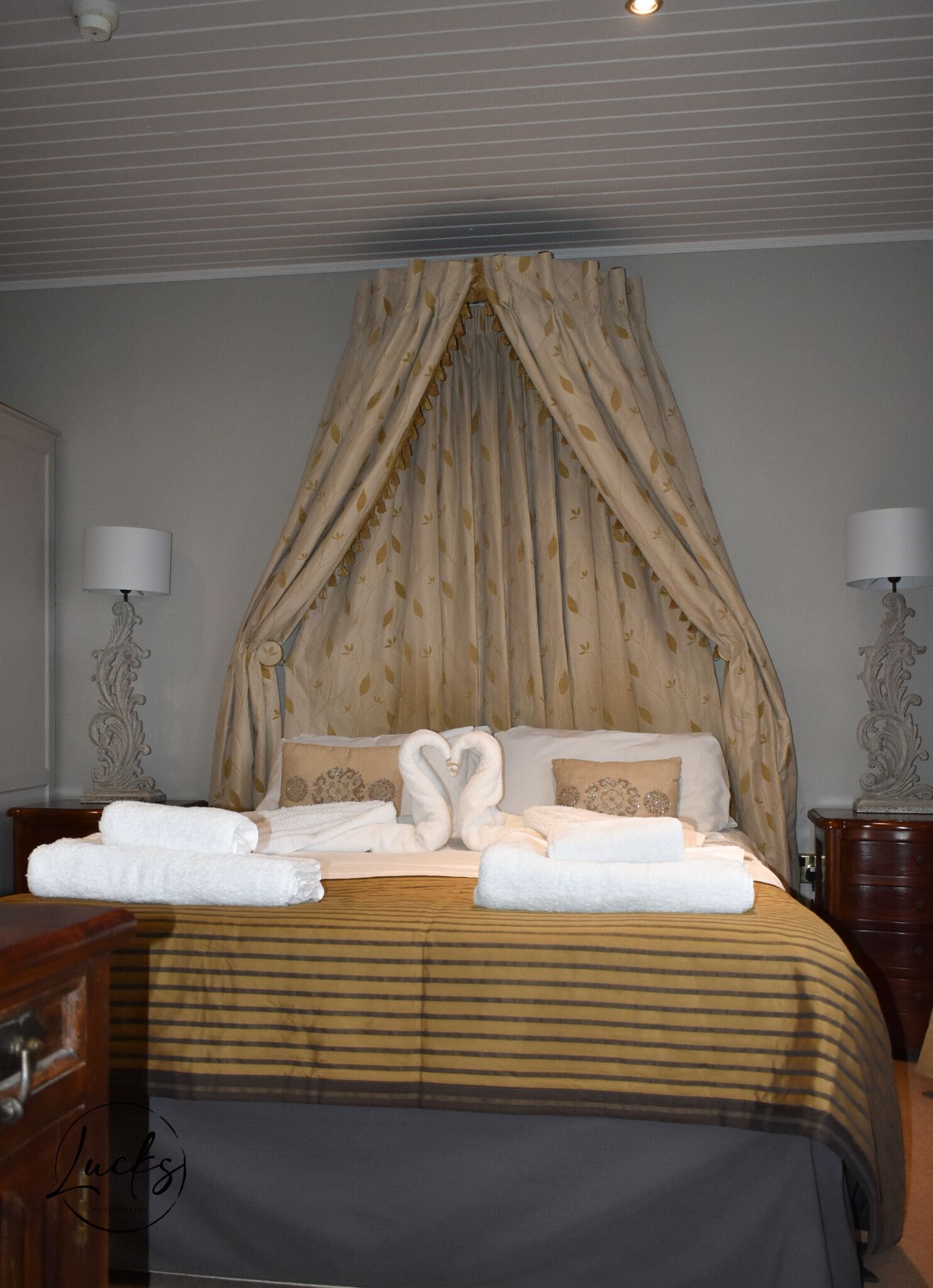 Una habitación de hotel con cama con dosel, dos lámparas de noche y toallas ordenadas sobre la cama.