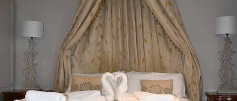 Una habitación de hotel con cama con dosel, dos lámparas de noche y toallas ordenadas sobre la cama.
