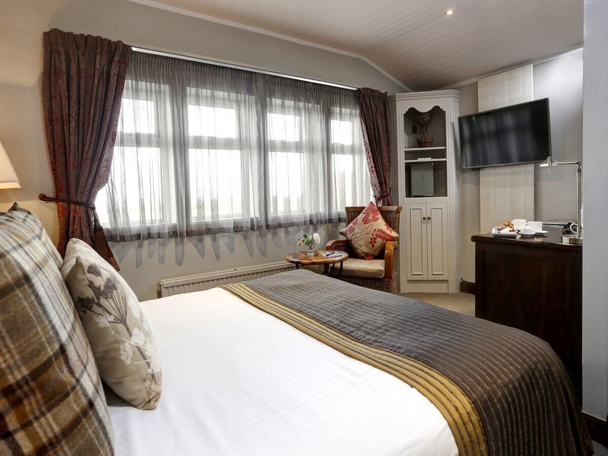 A hotel room with a large bed, a television, a desk with a chair, and a window with curtains.