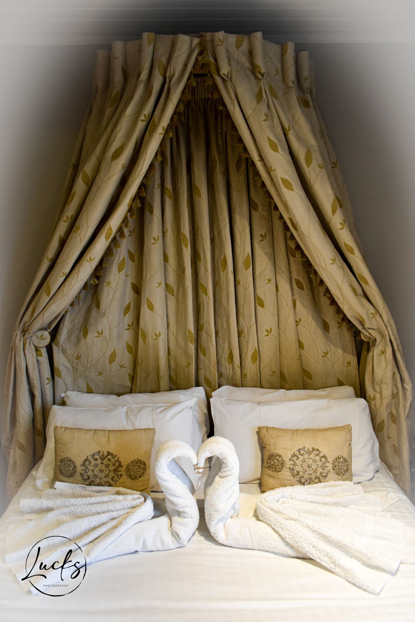 A bedroom with a canopy bed, two pillows with decorative patterns, and a swan-shaped towel arrangement.