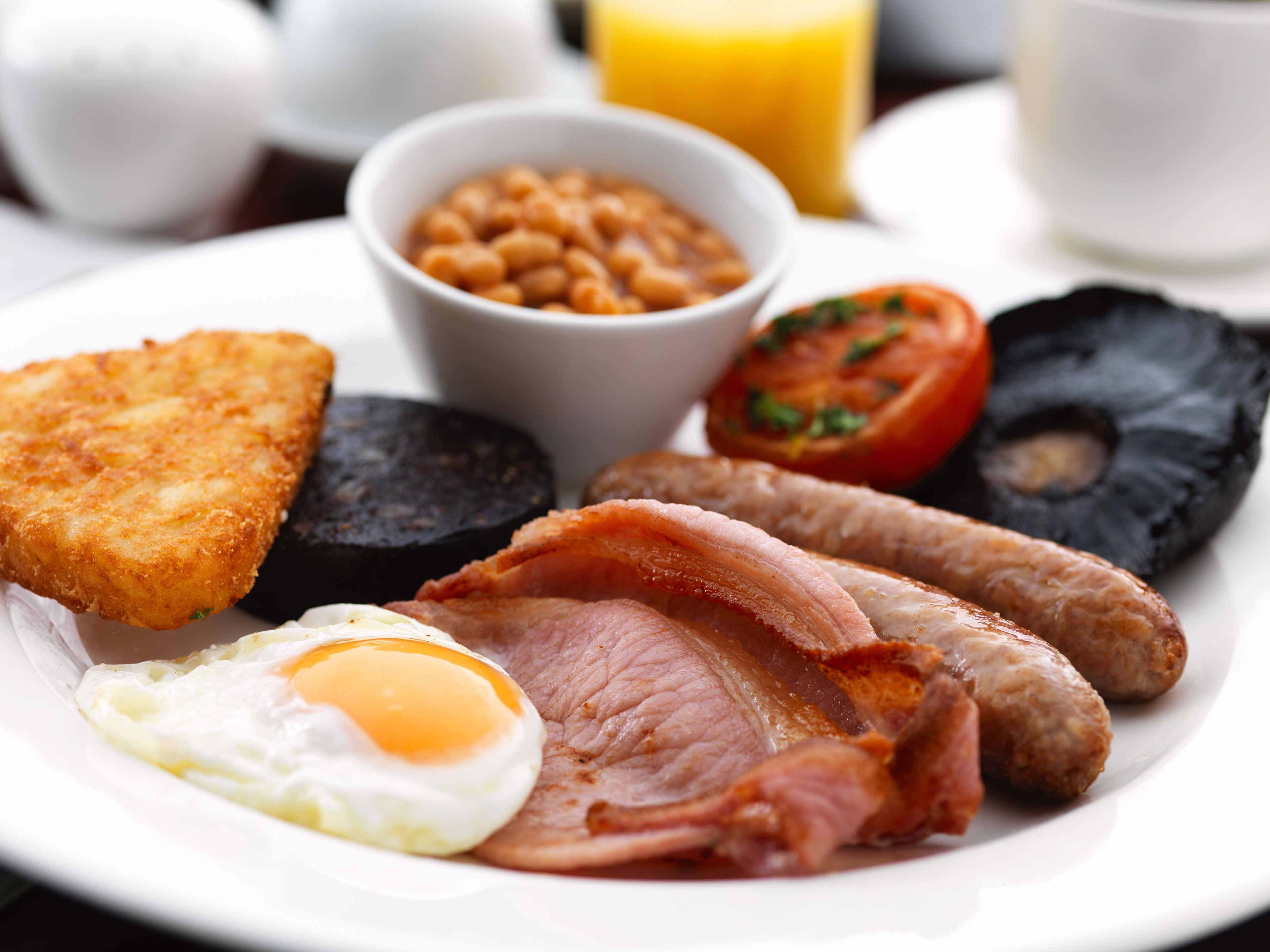 Un plato de desayuno con huevos, tocino, salchichas, morcilla, frijoles en salsa, tomate frito y tostadas.