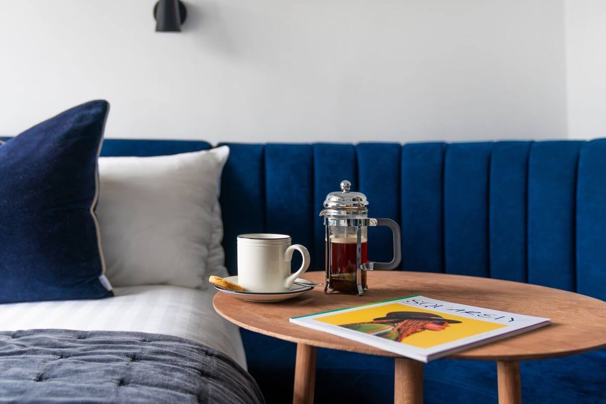A cozy room with a blue sofa, a small wooden table with a coffee pot, a mug, and a magazine.