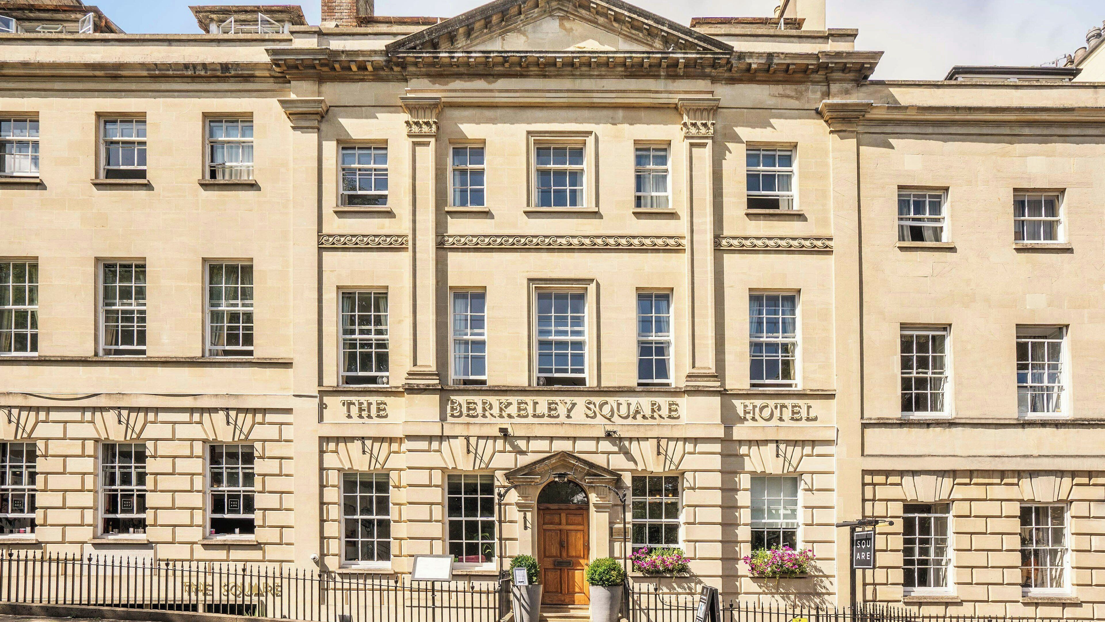 A historic building with a classic architectural style, featuring a prominent entrance with a wooden door and a sign reading 'The Berkeley Square Hotel.'