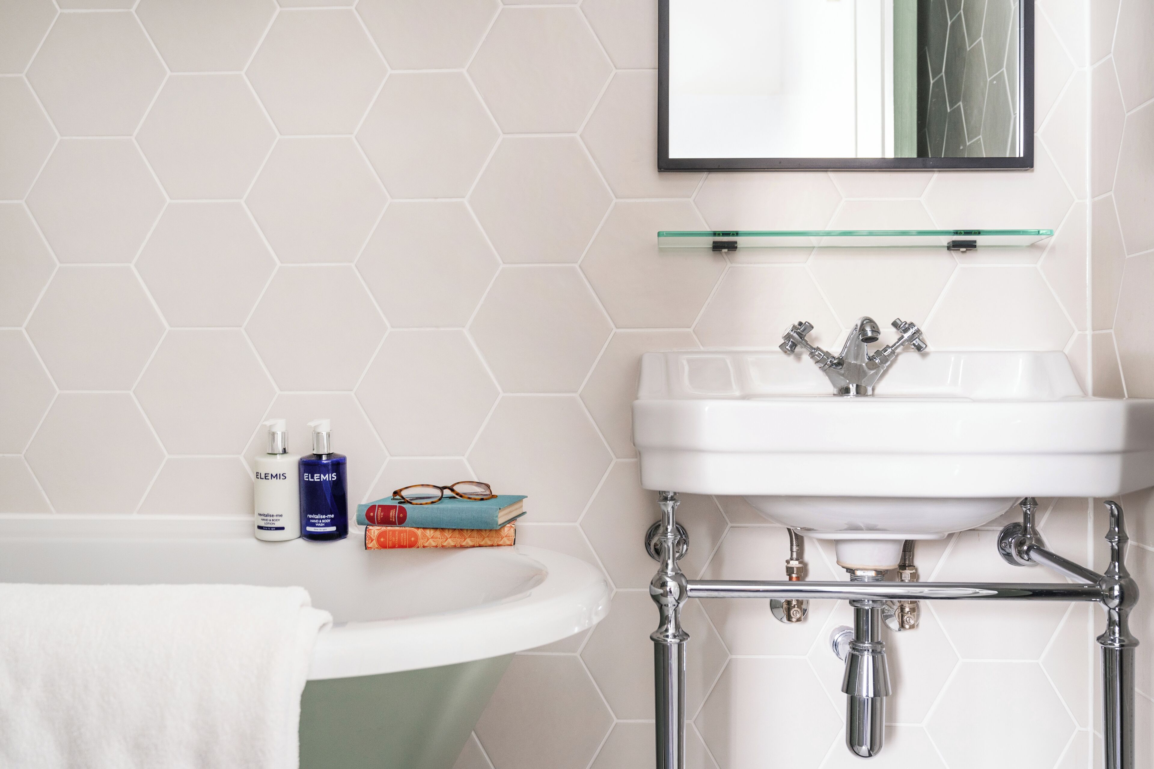 Um banheiro com pia branca, prateleira de vidro acima e parede com azulejos hexagonais.
