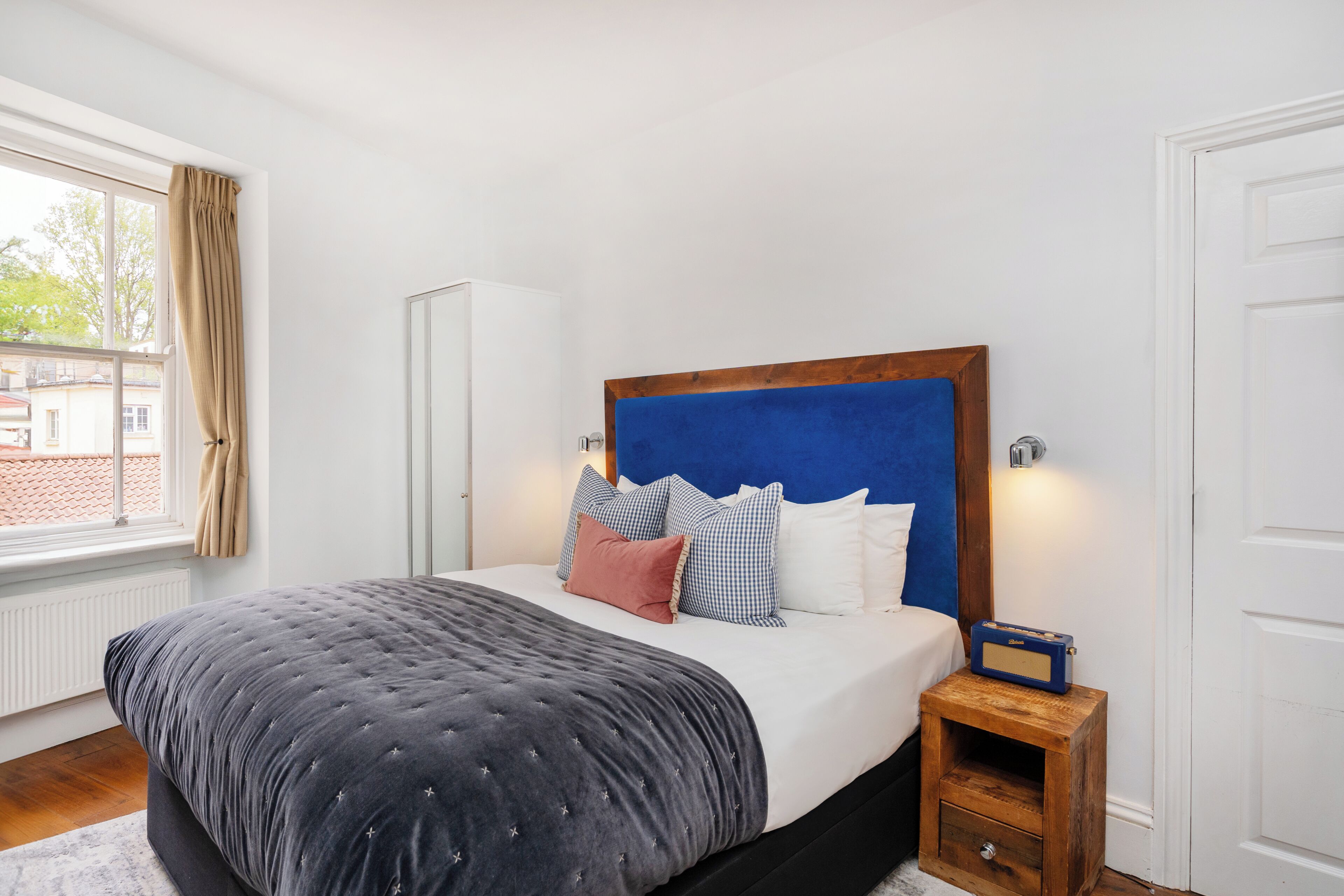 Une chambre à coucher comprenant un lit, une table de chevet, une armoire et une fenêtre avec des rideaux.