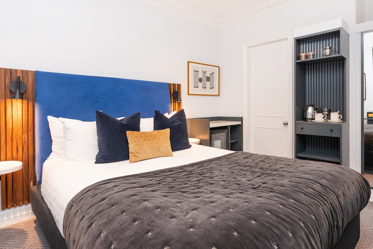A modern hotel room with a large bed, a bedside table, a wardrobe, and a framed picture on the wall.