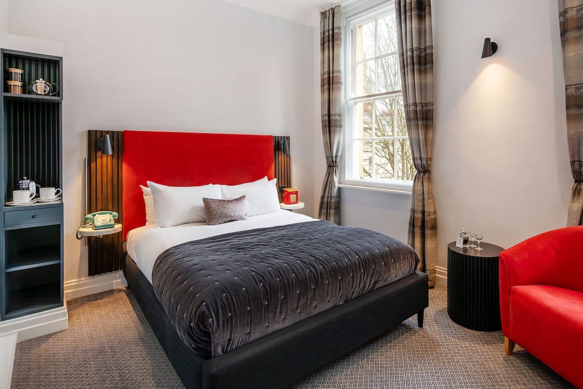 A modern bedroom with a large bed, a red chair, a small side table, and a window with curtains.