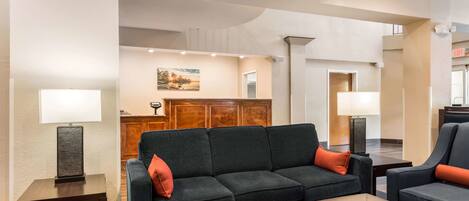 Un vestíbulo de hotel con un sofá de color oscuro, un mostrador de recepción de madera y un cuadro grande en la pared.