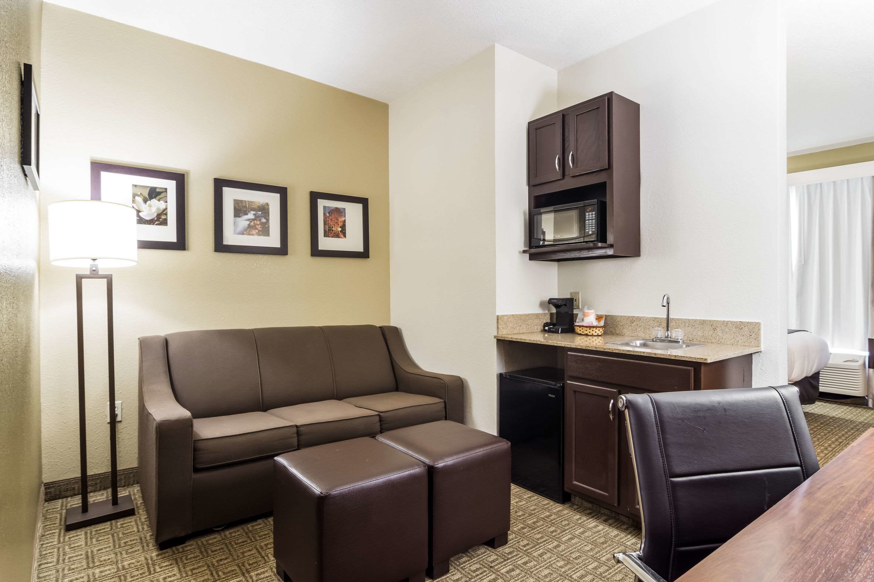 A compact hotel room with a sofa, ottoman, kitchenette, and a dining area.