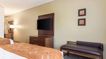 A hotel room with two beds, a flat-screen TV, a bench, and two framed pictures on the wall.