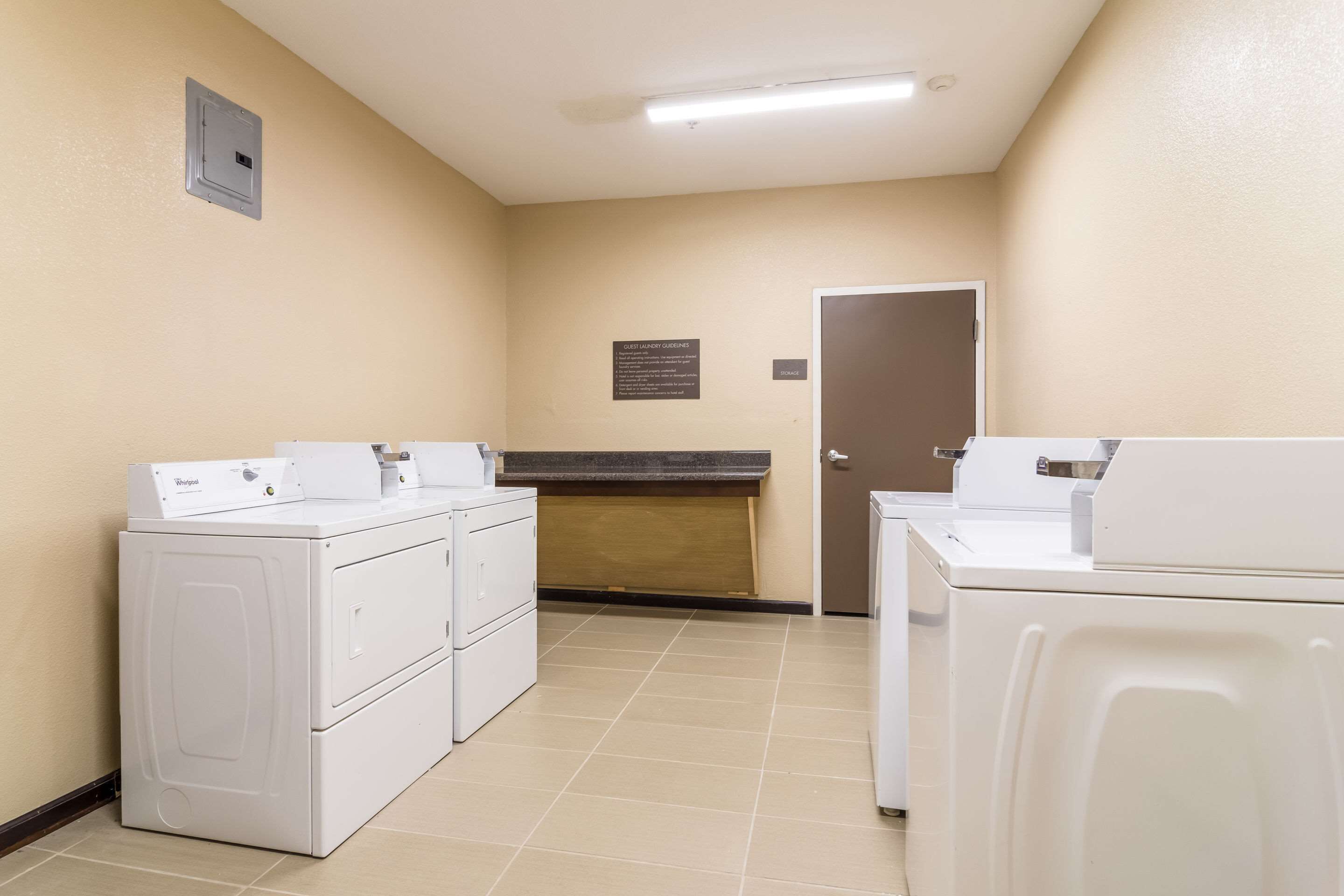 A laundry room with two white Whirlpool washers and dryers, a tiled floor, and a door with a sign above it.