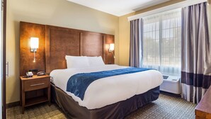 A hotel room with a large bed, bedside lamps, a nightstand, an air conditioning unit, and a window with curtains. - Comfort Suites Eufaula North (Eufaula)