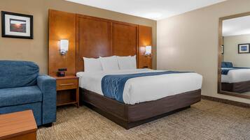 A hotel room with a large bed, a blue armchair, a bedside table, and a nightstand.