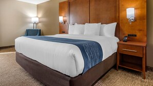 A hotel room with a large bed, wooden headboard, bedside lamps, and a nightstand with a phone. - Comfort Inn Birmingham - Irondale (Birmingham)