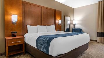 A hotel room with a large bed, wooden headboard, bedside tables with lamps, and a nightstand with a clock.